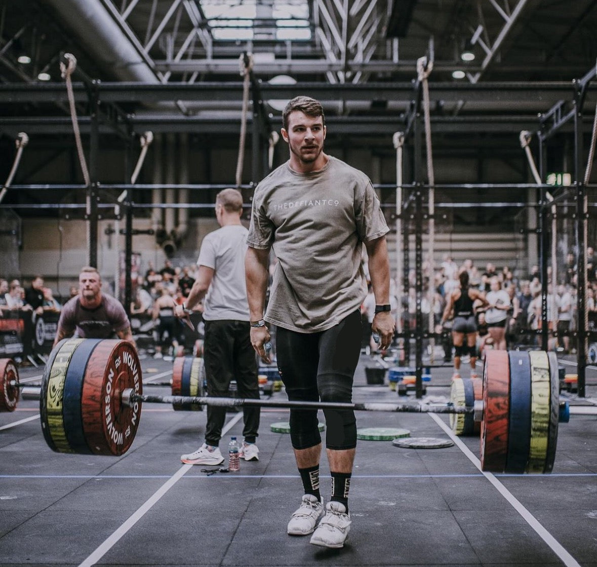 A photo showing a guy wearing an oversized The Defiant Co T-Shirt. The shirt has the famous ‘The Defiant Co’ logo across the front of the chest. The shirt has a round neck and is oversized. This particular version has a washed finish and is the colour Asphalt.