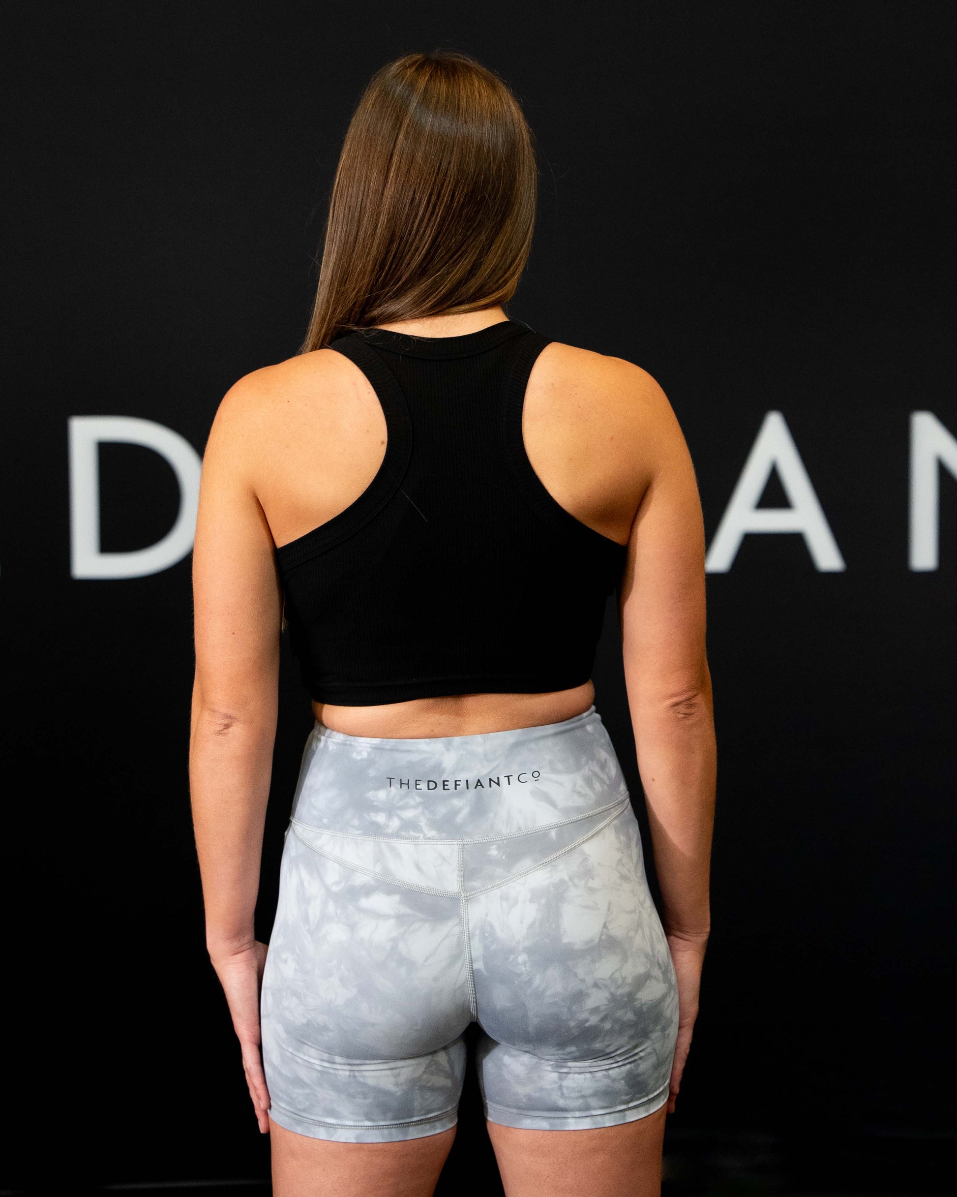 A girl against a black The Defiant Co backdrop wearing the DFNT. Ribbed Cropped Tank.  The tank is breathable with a stretchy fabric so is perfect for working out in.  It has a subtle DFNT. logo on a tag.  The colour is black.