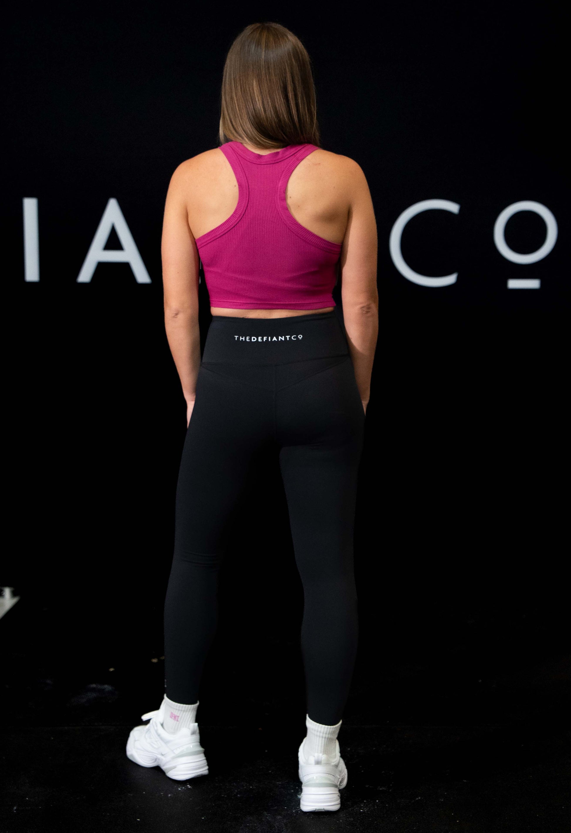 A girl against a black The Defiant Co backdrop wearing the DFNT. Ribbed Cropped Tank.  The tank is breathable with a stretchy fabric so is perfect for working out in.  It has a subtle DFNT. logo on a tag.  The colour is orchid.