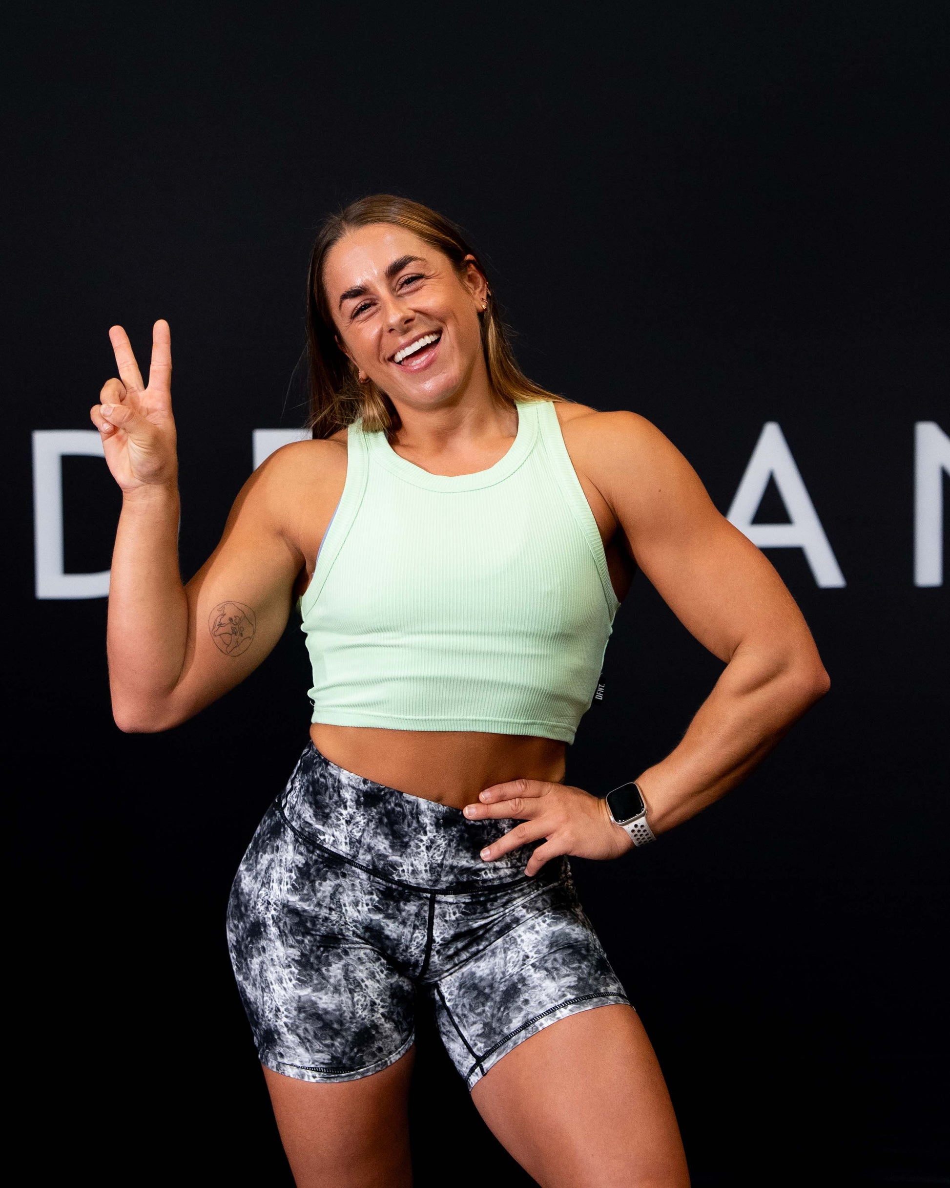 A girl against a black The Defiant Co backdrop wearing the DFNT. Ribbed Cropped Tank.  The tank is breathable with a stretchy fabric so is perfect for working out in.  It has a subtle DFNT. logo on a tag.  The colour is lime.