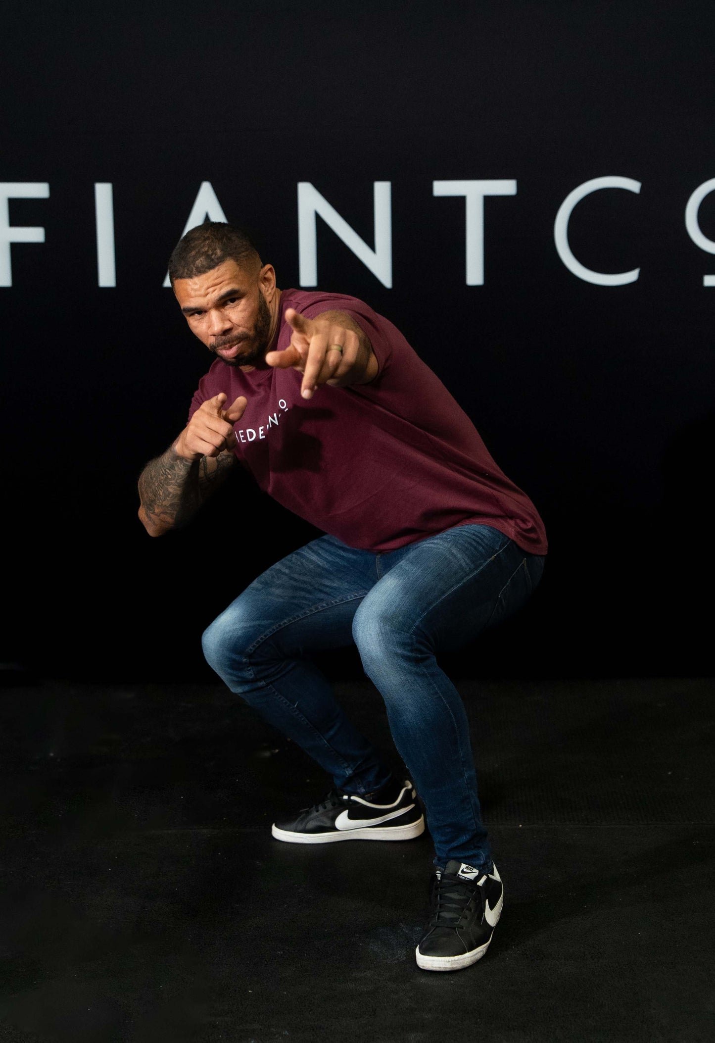A guy against a black The Defiant Co backdrop wearing the oversized t-shirt.  The tee has the famous 'The Defiant Co' logo boldly displayed across the front. The colour is burgundy.