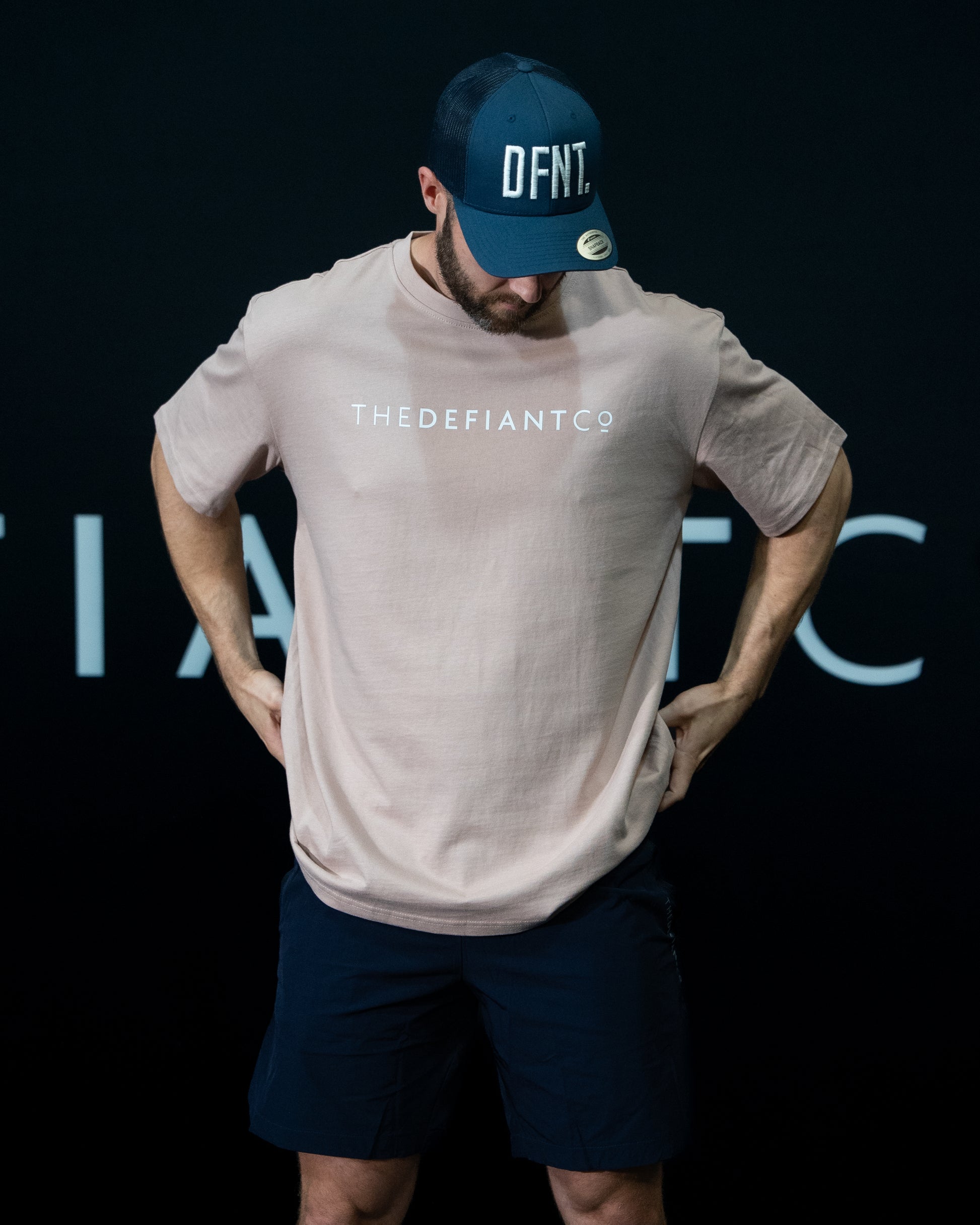 A guy against a black The Defiant Co backdrop wearing the oversized t-shirt.  The tee has the famous 'The Defiant Co' logo boldly displayed across the front. The colour is mauve.