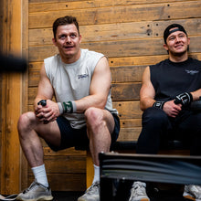 Load image into Gallery viewer, Two guys sat resting between workouts wearing the popular Proudly Refusing To Obey Authority Sleeveless Tees.  One is an off-white (bone) colour and the other is a faded black.