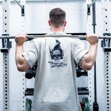 Load image into Gallery viewer, A guy weightlifting wearing the oversized Proudly Refusing To Obey Authority T-Shirt. The guys has big arms and a visible tattoo that matches the defiance of the message on the shirt.