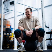 Load image into Gallery viewer, A guy sat resting between workouts wearing the faded khaki Proudly Refusing To Obey Authority Oversized T-Shirt. The guys is smiling and having a good time as he clearly loves his shirt.