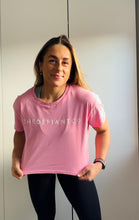 Load image into Gallery viewer, A girl wearing a cropped t-shirt .  The shirt is a female git and has a round neck and standard sleeve length.  The shirt has The Defiant Co logo across the centre of the chest.  The shirt is pink in colour.