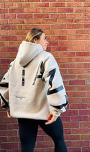 Load image into Gallery viewer, A girl stood in front of some brickwork in an amazing oversized hoodie! The hoodie is off-white and has a bold back DEFIANT print in black that spans both arms and the top of the back. There is also embroidery on the back that reads &#39;Proudly Refusing To Obey Authority&#39; with 2018 in Roman numerals underneath that. The hoodies are designed to be quite oversized to provide you with that cosy feel.