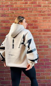 A girl stood in front of some brickwork in an amazing oversized hoodie! The hoodie is off-white and has a bold back DEFIANT print in black that spans both arms and the top of the back. There is also embroidery on the back that reads 'Proudly Refusing To Obey Authority' with 2018 in Roman numerals underneath that. The hoodies are designed to be quite oversized to provide you with that cosy feel.