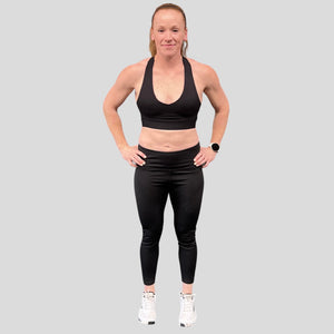 A photo showing the front of the amazing The Defiant Co Infinity Sports Bra.  The bra has a unique crossed back with The Defiant Co logo across both straps giving it a really standout look. The front is plain and simple giving it a really classy look. The colour is black.