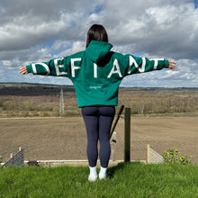 Load image into Gallery viewer, A girl stood in a garden with an incredible view with arms stretched wide in an amazing oversized hoodie! The hoodie is sea green and has a bold back DEFIANT print in white that spans both arms and the top of the back. There is also embroidery on the back that reads &#39;Proudly Refusing To Obey Authority&#39; with 2018 in Roman numerals underneath that. The hoodies are designed to be quite oversized to provide you with that cosy feel.