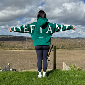 A girl stood in a garden with an incredible view with arms stretched wide in an amazing oversized hoodie! The hoodie is sea green and has a bold back DEFIANT print in white that spans both arms and the top of the back. There is also embroidery on the back that reads 'Proudly Refusing To Obey Authority' with 2018 in Roman numerals underneath that. The hoodies are designed to be quite oversized to provide you with that cosy feel.