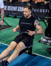 Load image into Gallery viewer, The photo shows a guy wearing The Defiant Co sleeveless t-shirt whilst rowing during a CrossFit workout.  The sleeveless is black and has the famous The Defiant Co logo across the front of the chest in white. The guy is an athlete competing at The Defiant Games.