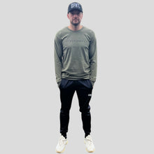 Load image into Gallery viewer, A photo showing ‘The Defiant Co’ long sleeved unisex t-shirt. The shirt has the famous ‘The Defiant Co’ logo across the front of the chest.  The shirt has a round neck and is slightly oversized. The shirt colour is olive green.