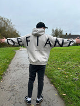 Load image into Gallery viewer, A guy stood in a park with arms stretched wide in an amazing oversized hoodie! The hoodie is off-white and has a bold back DEFIANT print in black that spans both arms and the top of the back. There is also embroidery on the back that reads &#39;Proudly Refusing To Obey Authority&#39; with 2018 in Roman numerals underneath that. The hoodies are designed to be quite oversized to provide you with that cosy feel.