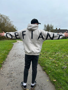 A guy stood in a park with arms stretched wide in an amazing oversized hoodie! The hoodie is off-white and has a bold back DEFIANT print in black that spans both arms and the top of the back. There is also embroidery on the back that reads 'Proudly Refusing To Obey Authority' with 2018 in Roman numerals underneath that. The hoodies are designed to be quite oversized to provide you with that cosy feel.