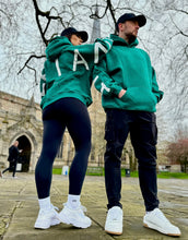Load image into Gallery viewer, A guy and a girl stood posing in front of a church on a cloudy day, both dressed in the amazing Oversized DFNT. Eternity Hoodies.  The Hoodies have a plain front with a big DEFIANT lettering across the arms and back, a subtle DFNT. tag on the left side and then embroidery stating Proudly Refusing To Obey Authority under the large lettering as well as The Defiant Co embroidered to the left sleeve cuff.  The hoodies are sea green with white logos.
