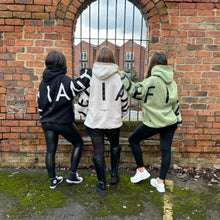 Load image into Gallery viewer, Three girls on a bridge overlooking a canal in amazing oversized hoodies! The hoodies are sage green, off-white and black respectively and have a bold back DEFIANT print that spans both arms and the top of the back. There is also embroidery on the back that reads &#39;Proudly Refusing To Obey Authority&#39; with 2018 in Roman numerals underneath that. The hoodies are designed to be quite oversized to provide you with that cosy feel.