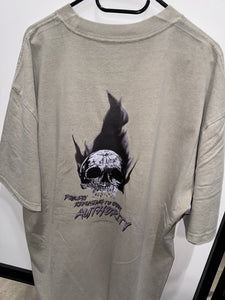 A photo showing the back of a unisex t-shirt.  The shirt has a big bold print on the back of a skull in flames. Underneath the skull is the defiant tag line 'Proudly Refusing To Obey Authority' with the The Defiant Co logo under that. The t-shirt is faded eucalyptus in colour.