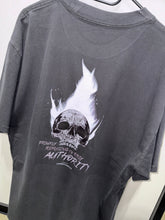 Load image into Gallery viewer, A photo showing the back of a unisex t-shirt.  The shirt has a big bold print on the back of a skull in flames. Underneath the skull is the defiant tag line &#39;Proudly Refusing To Obey Authority&#39; with the The Defiant Co logo under that. The t-shirt is faded coal in colour.