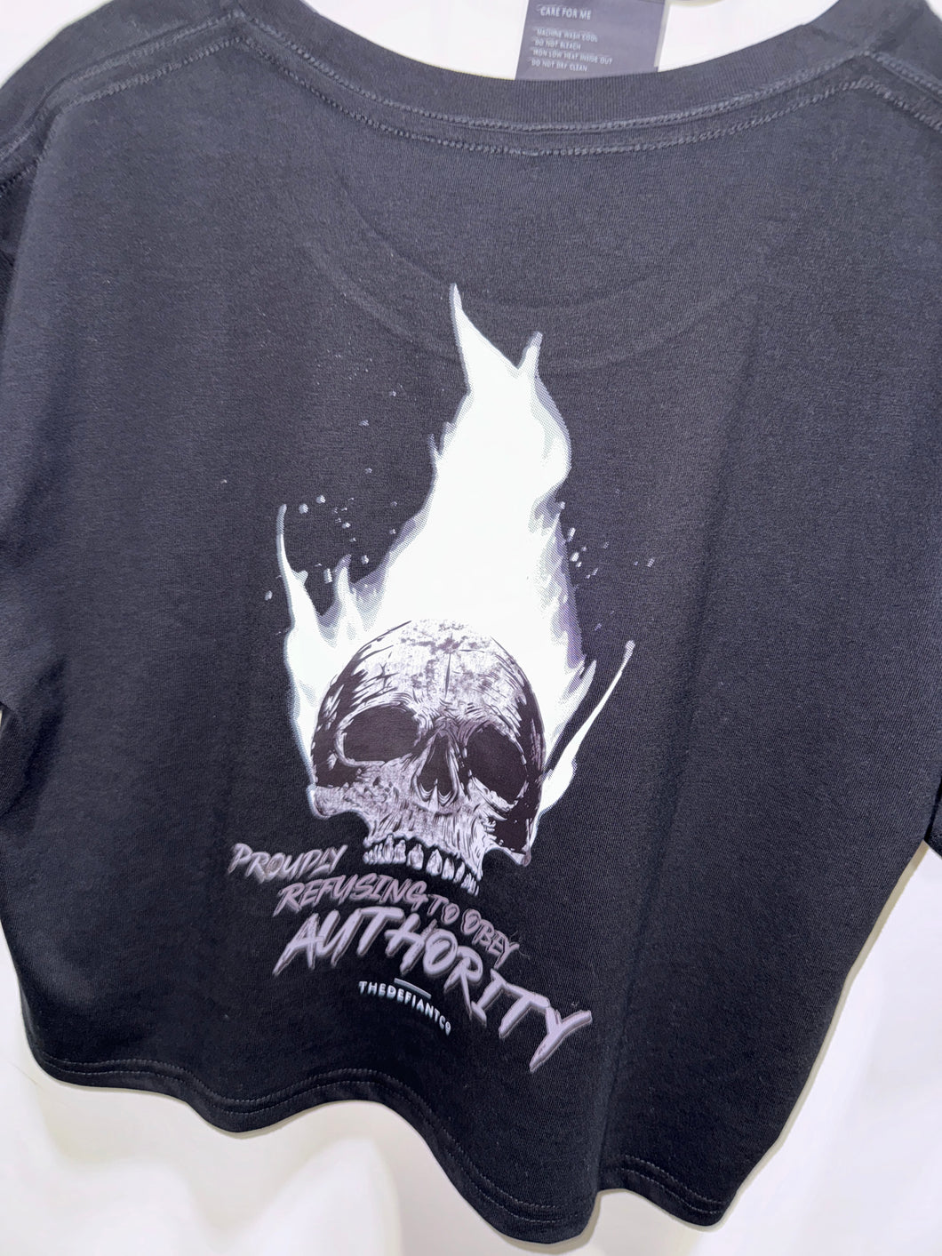A photo showing the back of a female fit cropped t-shirt.  The shirt has a big bold print on the back of a skull in flames. Underneath the slull is the defiant tag line 'Proudly Refusing To Obey Authority' with the The Defiant Co logo under that. The shirt is black in colour.