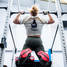Load image into Gallery viewer, A girl doing Chest to Bar pull ups wearing an ecru cropped t-shirt with a bold graphic desiign of a skull in flames large on the back. The girl is also wearing dark olive green leggings with The Defiant Co logo across the waistband.