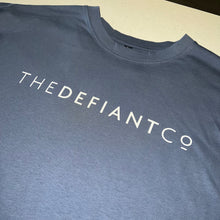 Load image into Gallery viewer, A photo showing an oversized The Defiant Co T-Shirt.  The shirt has the famous ‘The Defiant Co’ logo across the front of the chest.  The shirt has a round neck and is oversized.  This particular version is the colour steel blue.