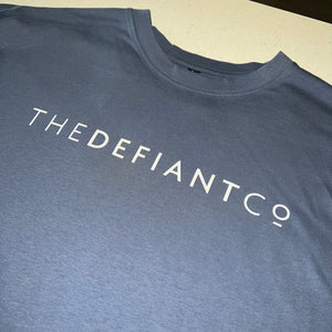 A photo showing an oversized The Defiant Co T-Shirt.  The shirt has the famous ‘The Defiant Co’ logo across the front of the chest.  The shirt has a round neck and is oversized.  This particular version is the colour steel blue.
