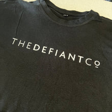 Load image into Gallery viewer, A photo showing an oversized The Defiant Co T-Shirt.  The shirt has the famous ‘The Defiant Co’ logo across the front of the chest.  The shirt has a round neck and is oversized.  This particular version is black.