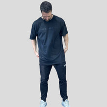 Load image into Gallery viewer, A photo showing a guy wearing an oversized The Defiant Co T-Shirt.  The shirt has the famous ‘The Defiant Co’ logo across the front of the chest.  The shirt has a round neck and is oversized.  This particular version has a washed finish and is the colour black with black print.