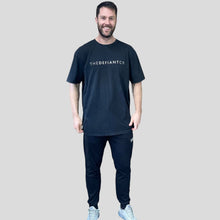 Load image into Gallery viewer, A photo showing a guy wearing an oversized The Defiant Co T-Shirt.  The shirt has the famous ‘The Defiant Co’ logo across the front of the chest.  The shirt has a round neck and is oversized.  This particular version has a washed finish and is the colour black.