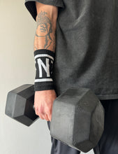 Load image into Gallery viewer, A guy holding a dumbbell wearing the DFNT. performance sweat bands.  The sweat bands are black with DFNT. in white incased in a white border.  The sweatbands are elasticated and will stand up to any workout.