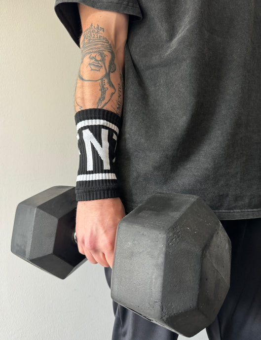 A guy holding a dumbbell wearing the DFNT. performance sweat bands.  The sweat bands are black with DFNT. in white incased in a white border.  The sweatbands are elasticated and will stand up to any workout.