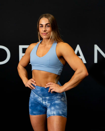 A girl against a black The Defiant Co backdrop wearing the Eternal 6 inch booty shorts.  The high waist and breathable material makes them perfect for any workout.  The blue cloud.