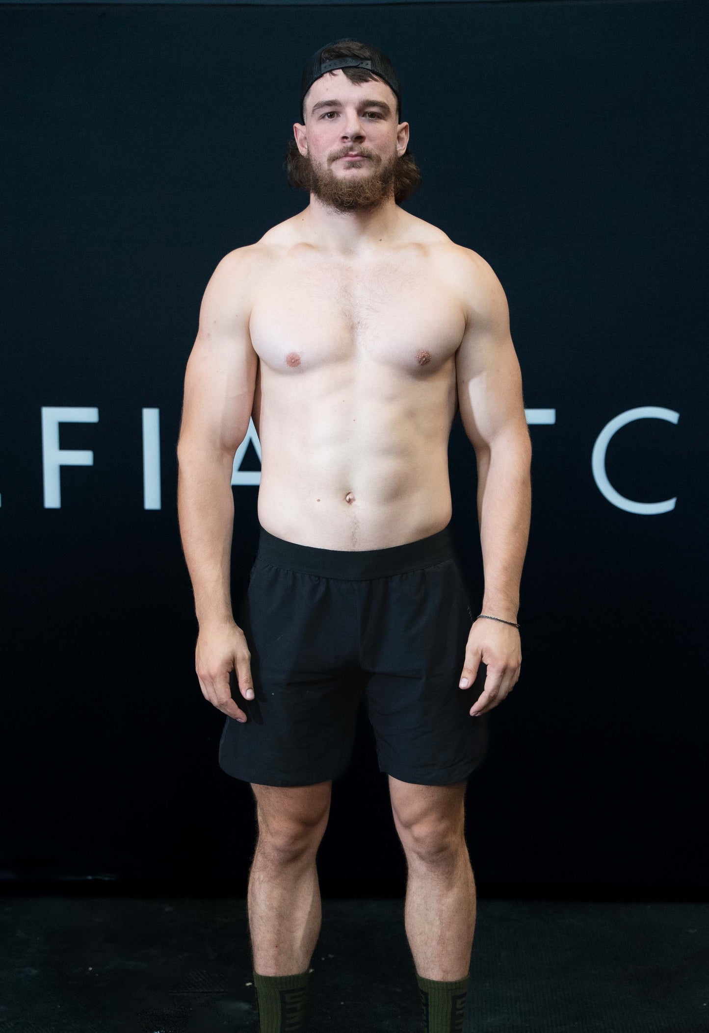 A man against a black The Defiant Co backdrop wearing the performance shorts with their draw string and elasticated black waist band.  The Defiant Co is subtly embossed down the right leg. The colour is black.