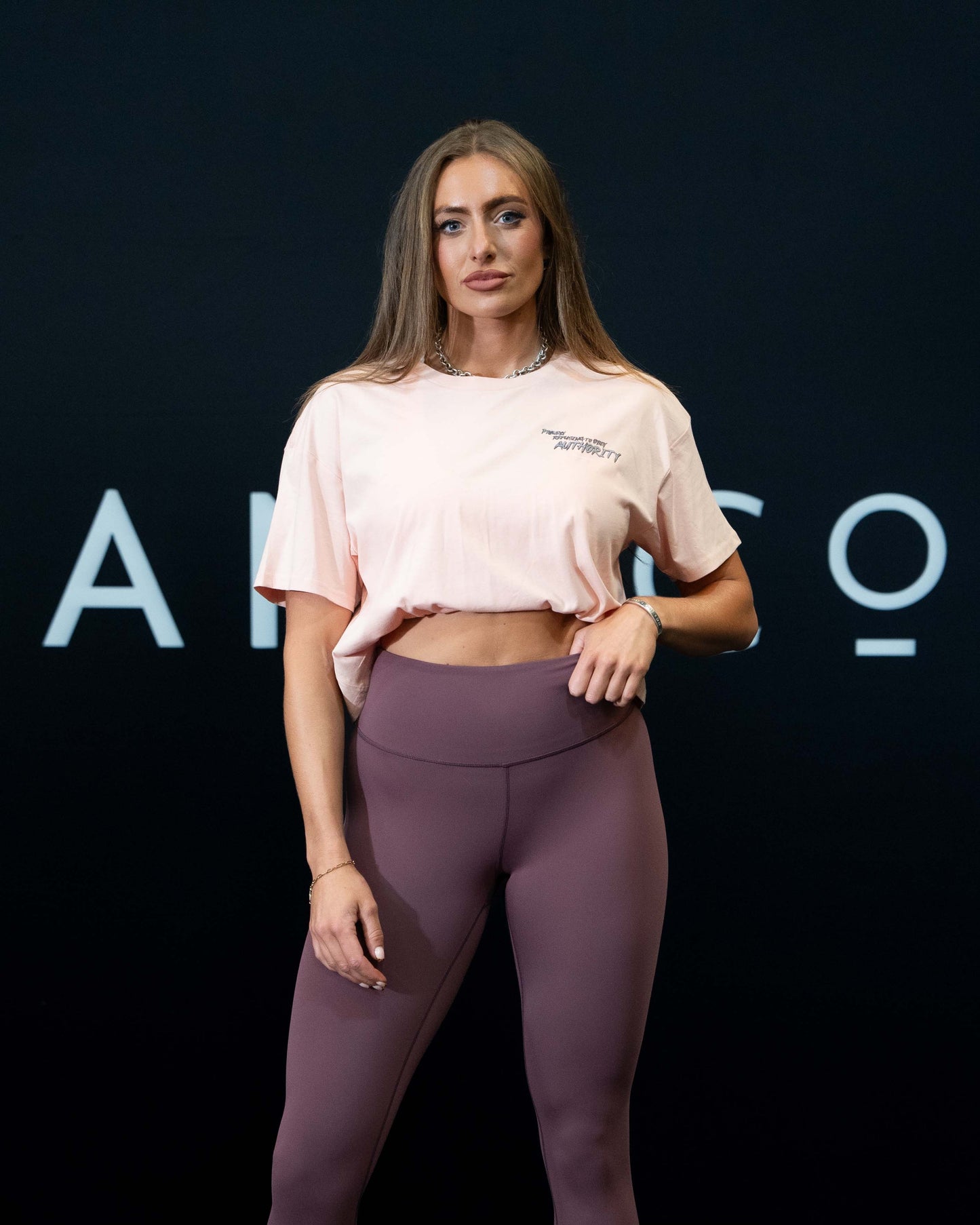 A girl against a black The Defiant Co backdrop wearing the proudly refusing to obey authority cropped t-shirt in blush with the burgundy TDCo performance leggings.