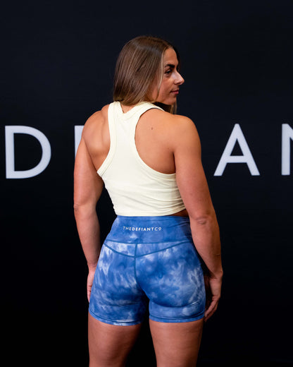 A girl against a black The Defiant Co backdrop wearing the DFNT. Ribbed Cropped Tank.  The tank is breathable with a stretchy fabric so is perfect for working out in.  It has a subtle DFNT. logo on a tag.  The colour is lemon.