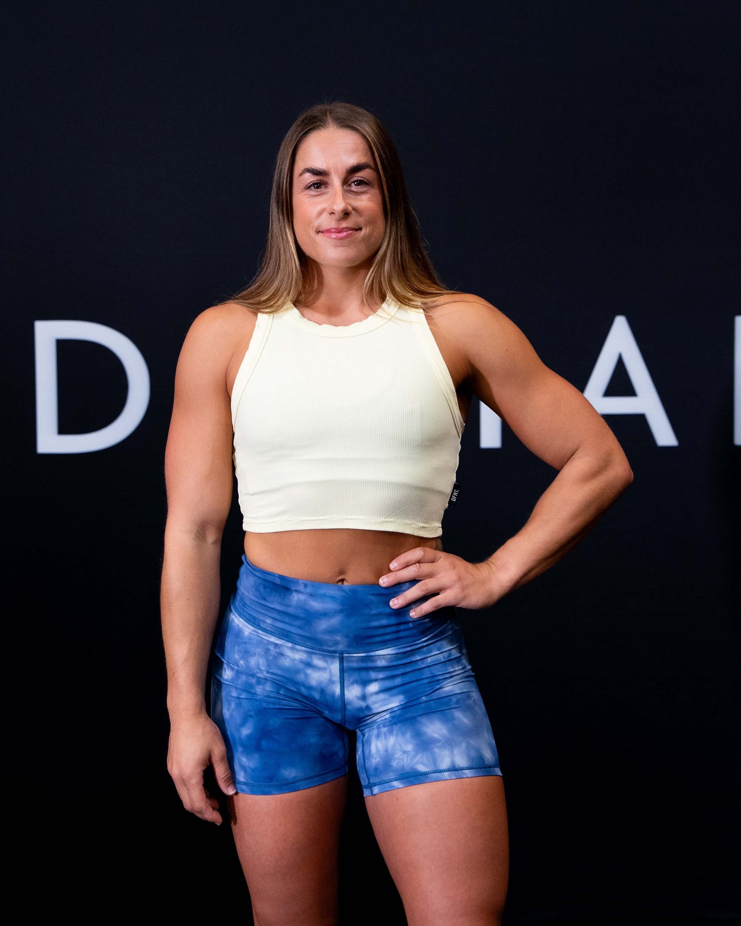 A girl against a black The Defiant Co backdrop wearing the DFNT. Ribbed Cropped Tank.  The tank is breathable with a stretchy fabric so is perfect for working out in.  It has a subtle DFNT. logo on a tag.  The colour is lemon.