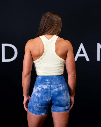 A girl against a black The Defiant Co backdrop wearing the DFNT. Ribbed Cropped Tank.  The tank is breathable with a stretchy fabric so is perfect for working out in.  It has a subtle DFNT. logo on a tag.  The colour is lemon.