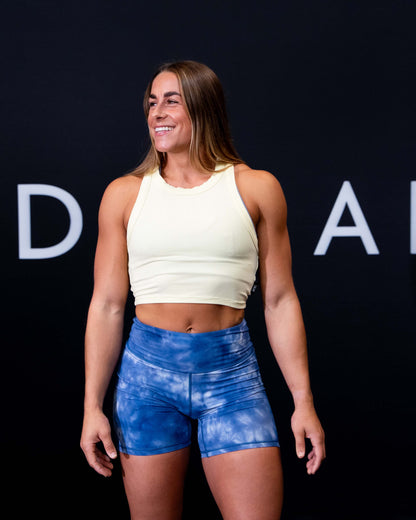 A girl against a black The Defiant Co backdrop wearing the DFNT. Ribbed Cropped Tank.  The tank is breathable with a stretchy fabric so is perfect for working out in.  It has a subtle DFNT. logo on a tag.  The colour is lemon.