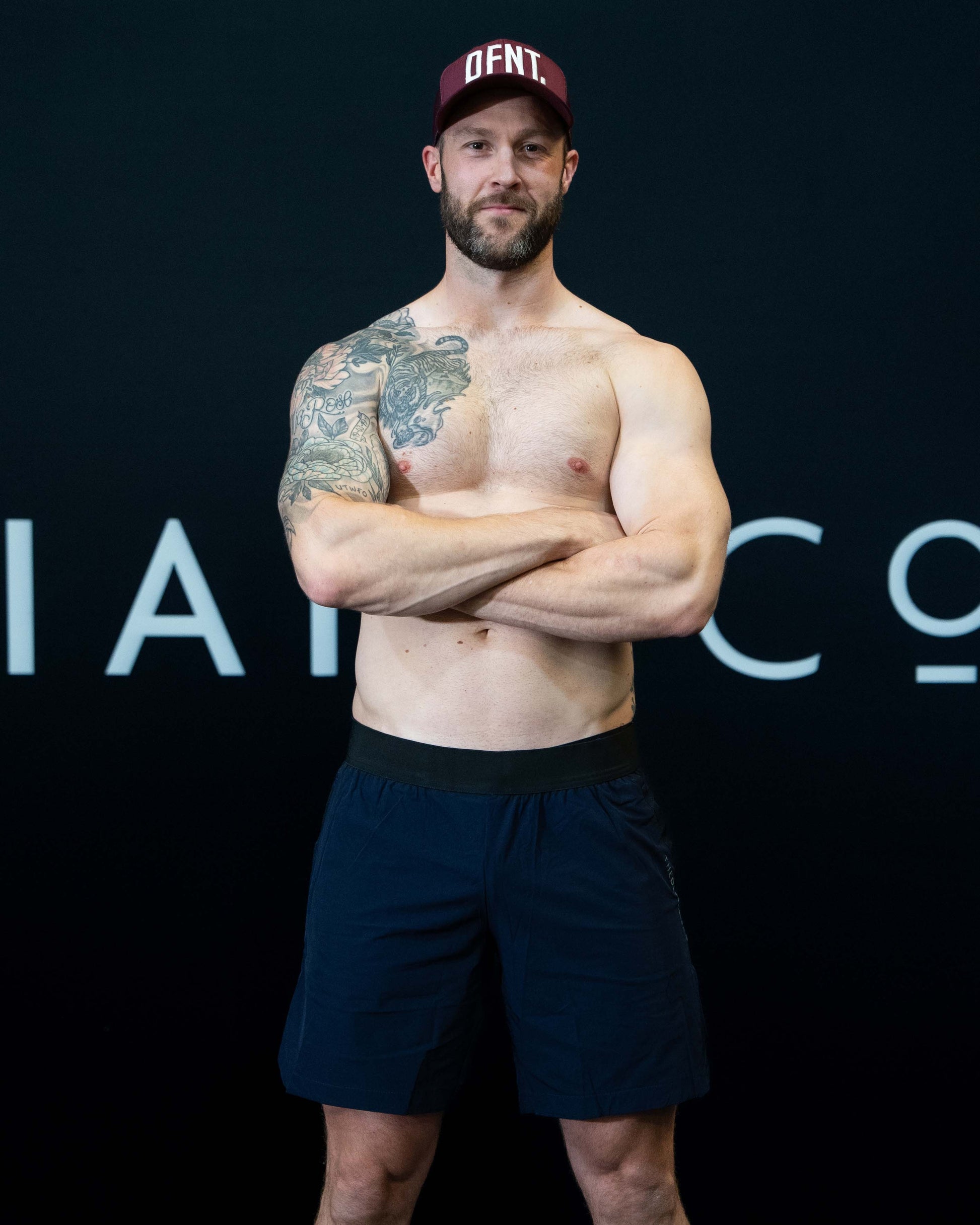 A man against a black The Defiant Co backdrop wearing the performance shorts with their draw string and elasticated black waist band.  The Defiant Co is subtly embossed down the right leg. The colour is navy blue.