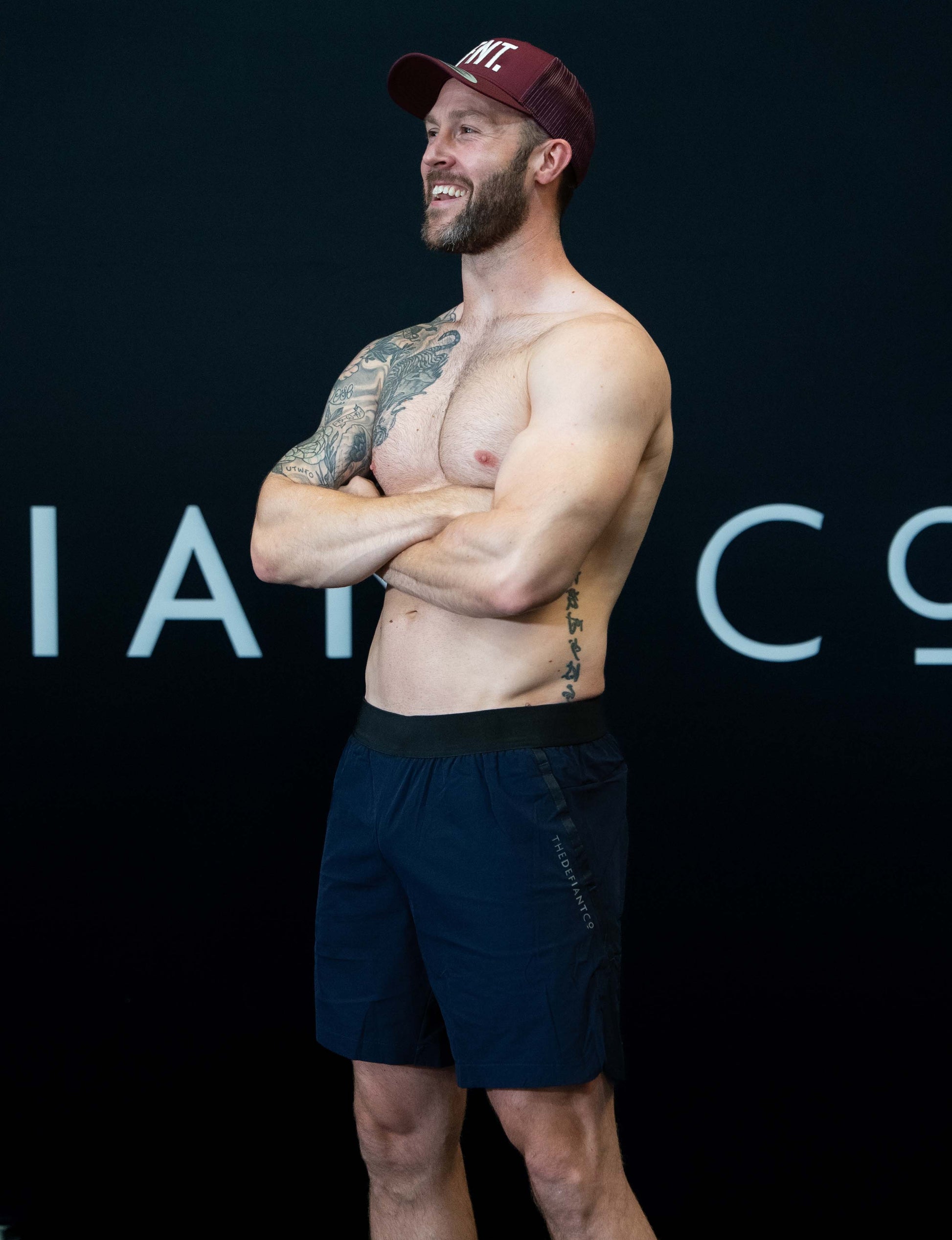 A man against a black The Defiant Co backdrop wearing the performance shorts with their draw string and elasticated black waist band.  The Defiant Co is subtly embossed down the right leg. The colour is navy blue.