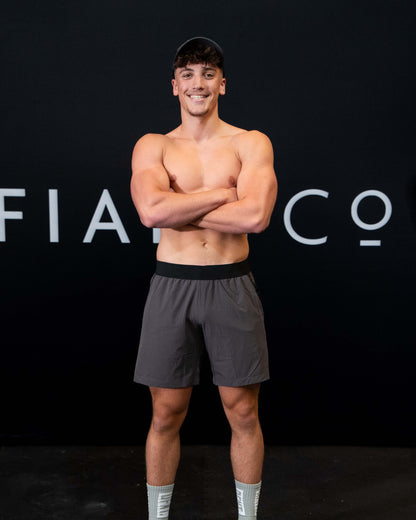 A man against a black The Defiant Co backdrop wearing the performance shorts with their draw string and elasticated black waist band.  The Defiant Co is subtly embossed down the right leg. The colour is charcoal grey.