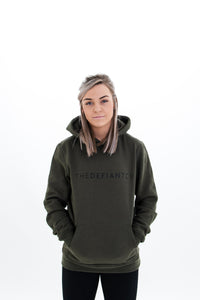 A girl wearing a standard fit, unisex The Defiant Co Hoodie.  The hoodie has draw strings and a pouch pocket on the front as per all standard designs.  The hoodie has the famous The Defiant Co logo across the front of the chest and is plain on the back.  The colour is olive green.